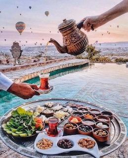 Turkish breakfast tray by a pool with poured tea and hot air balloons in the distance