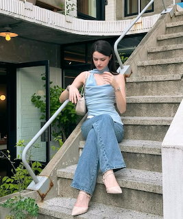 Woman in a light blue top and jeans sitting on concrete stairs outdoors
