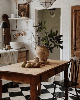 Rustic wooden kitchen table with pears and a vase of branches on black and white checkered floor