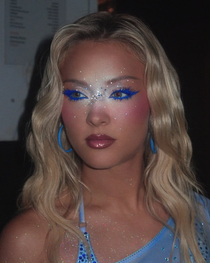 Woman with blonde hair wearing blue glitter eye makeup and blue beaded jewelry