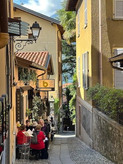 Narrow alley in Bellagio with yellow buildings, cobblestones, and people seated outside a cafe
