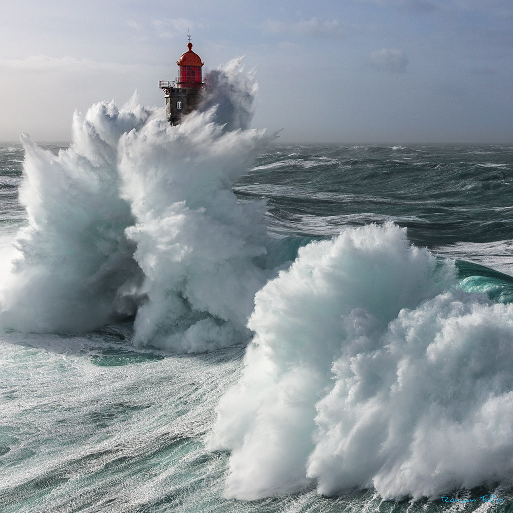 Red lighthouse tower engulfed by huge crashing ocean waves during violent storm