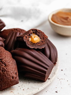 Chocolate-glazed madeleines on a speckled plate, one cut open revealing caramel filling