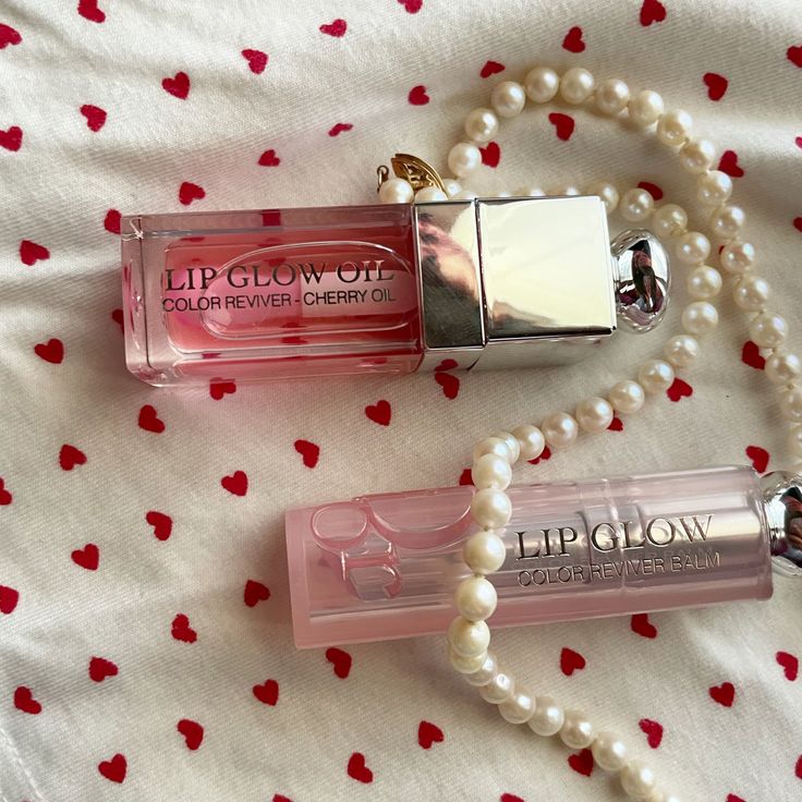 Pink lip gloss tubes with pearl necklace on white fabric decorated with tiny red hearts