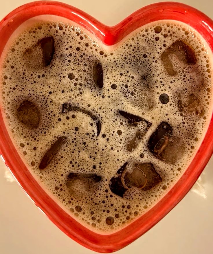 Iced coffee with ice cubes in red heart-shaped mug, viewed from above