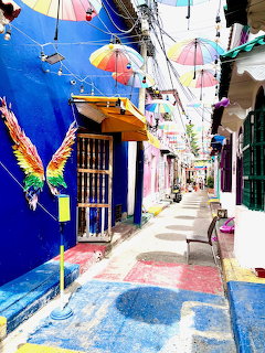 Colorful Cartagena street with umbrellas overhead and a wing mural on a blue wall