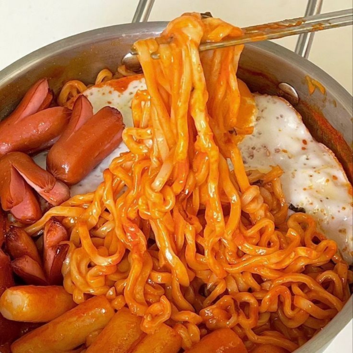 Spicy ramen noodles in a pot with sausages, rice cakes, and fried eggs