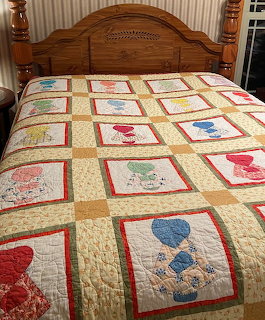 Handmade patchwork quilt with Sunbonnet Sue blocks in various colors on bed with wooden headboard