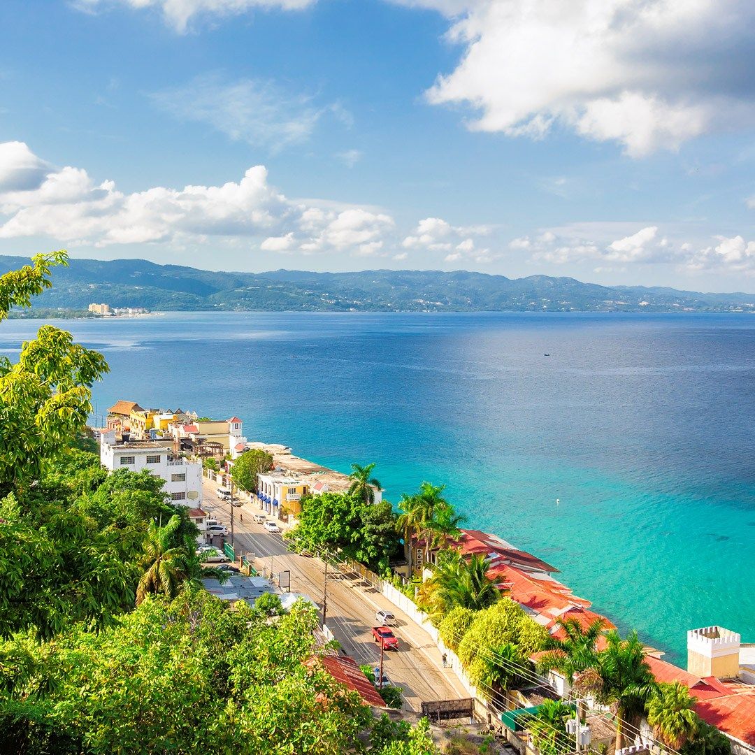 Tropical Jamaica coastline with turquoise water, palm trees, green hills, and distant mountains