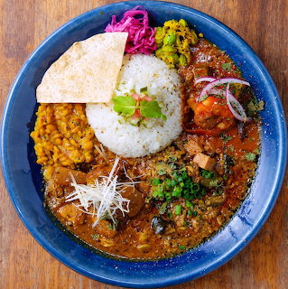 Asian curry rice bowl with white rice center, multiple curries, lentils, pickled cabbage, and garnishes on blue plate