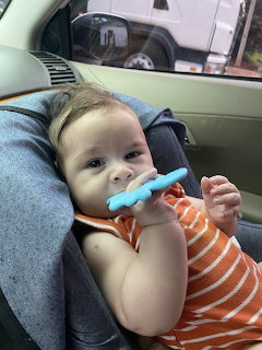 Baby in orange striped shirt sitting in car seat chewing a blue teething toy