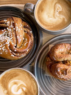 Overhead view of lattes with cinnamon buns and pastries on a wooden table