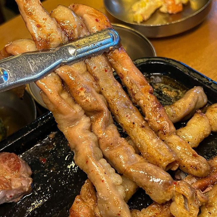 Grilled gopchang Korean beef intestines on grill with tongs