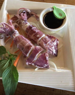Sliced squid served on a white plate with dark dipping sauce and green garnish