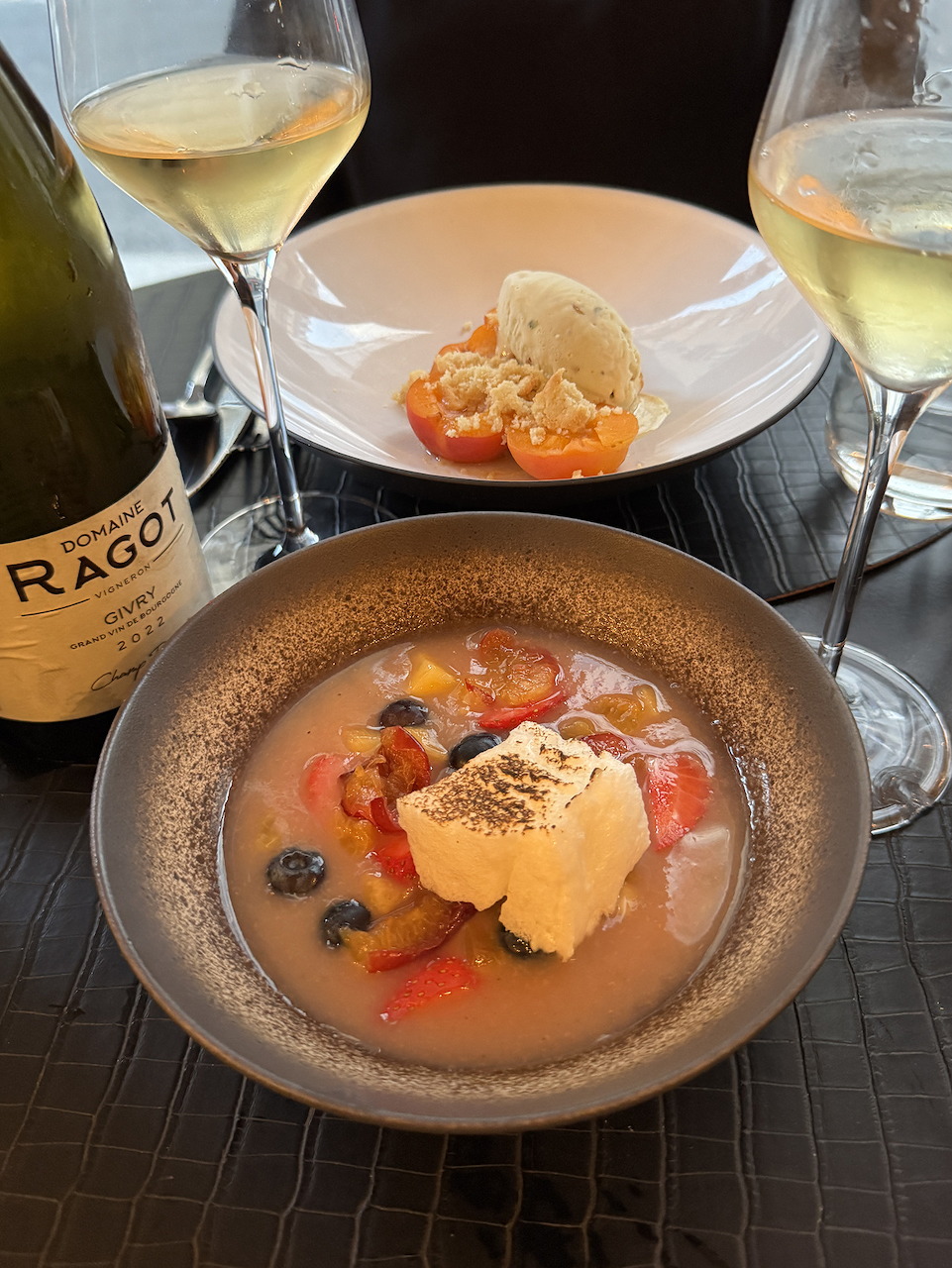 Restaurant table with a bowl of fish in tomato broth, a dessert plate, and white wine glasses
