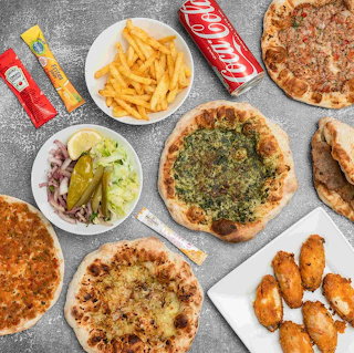 Overhead spread of flatbreads, fries, wings, wrap, salad, sauces, and a cola can on a table