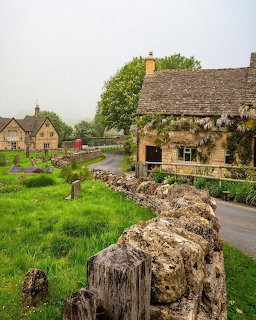 Rustic stone cottage by a country road with green field and stone wall