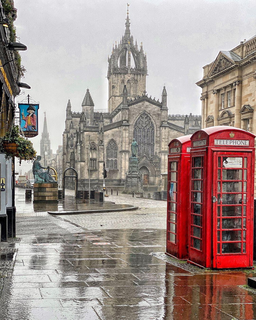 St Giles' Cathedral in Edinburgh with red British telephone box on rainy cobblestone street