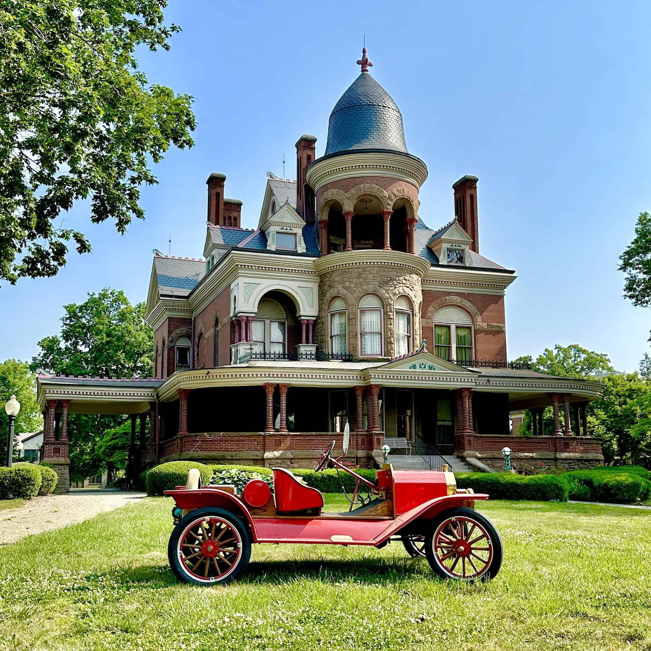 Vintage red car on the grass in front of a large historic mansion