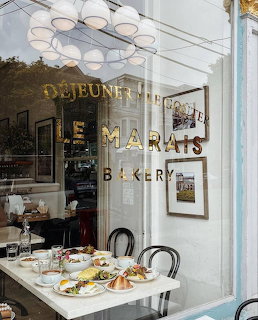 Window view of Le Marais Bakery with a table of pastries and dishes inside