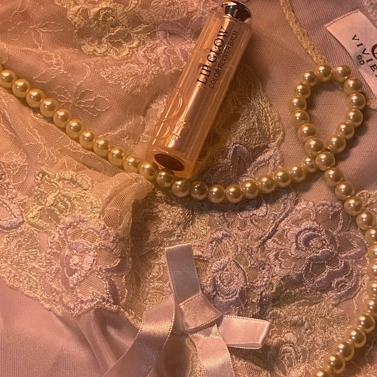 Pink perfume bottle with pearl necklace draped over lace fabric