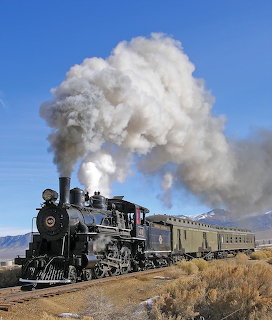 Black steam locomotive Nevada Northern 40 pulling passenger cars through a dry desert landscape
