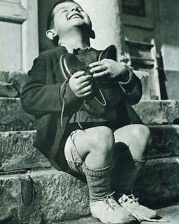 Black-and-white photo of a laughing boy sitting on stone steps holding shoes