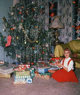 Girl in red dress sitting by Christmas tree with wrapped gifts in vintage home interior