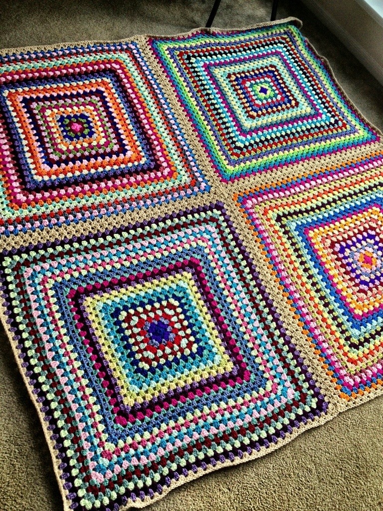 Four colorful crocheted granny squares arranged on a beige carpet