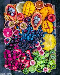 Overhead view of a colorful fruit platter with mango, dragon fruit, beries, kiwi, and citrus arranged in a rainbow pattern