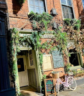 Brick cafe entrance with vines, chalkboard signs, and a white bicycle outside
