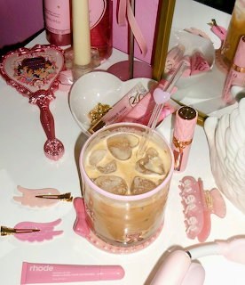Iced coffee with heart ice cubes surrounded by pink girly accessories on a table