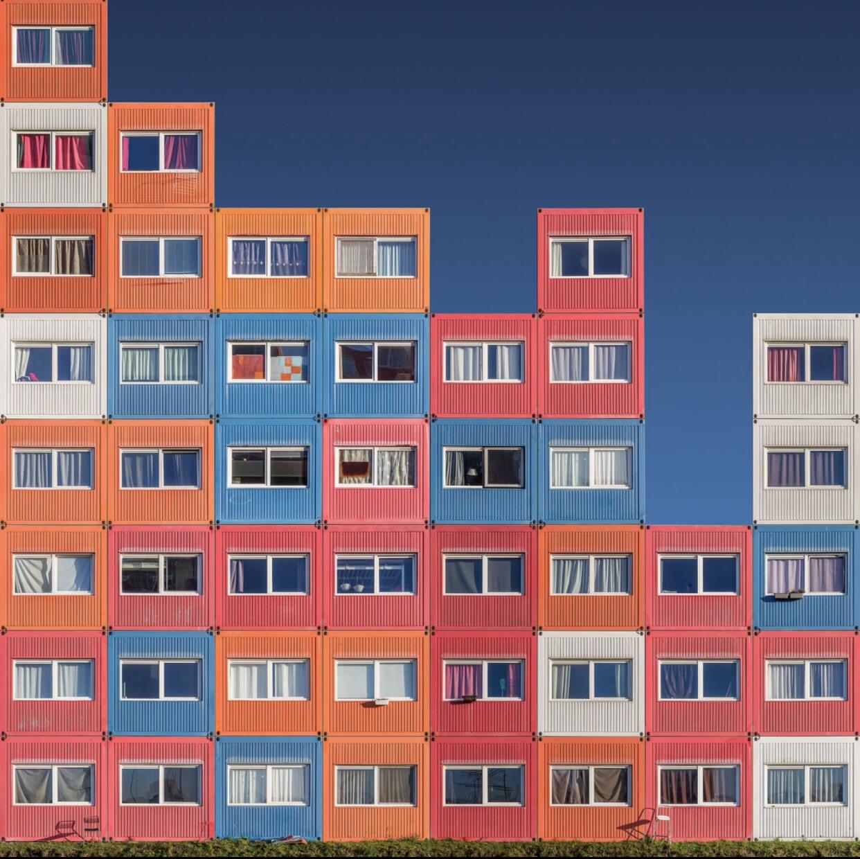 Colorful multi-story apartment buildings with orange, pink, and blue facades and uniform windows against blue sky