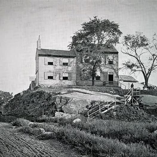 Black-and-white drawing of an old farmhouse on a hill with trees and a fence