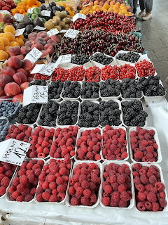 Market stall displaying containers of raspberries, blackberries, red currants, cherries, and peaches