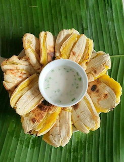Grilled banana slices arranged in a circle around a small bowl of white dipping sauce on a banana leaf