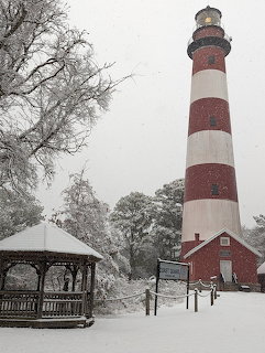 Red and white striped lighthouse in winter snow with gazebo and keeper's house