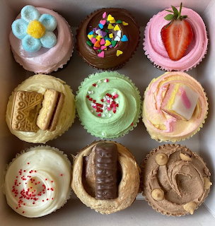 Overhead view of nine decorated cupcakes with various frosting colors and toppings in a box