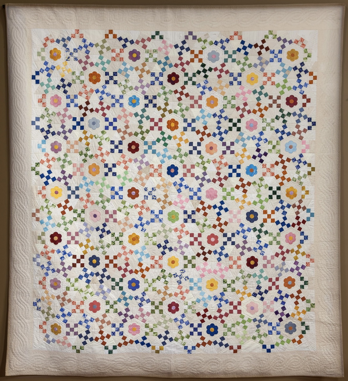 Framed quilt with colorful geometric floral and ring patterns on a pale background