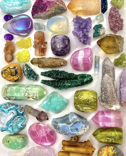Assorted polished gemstones and minerals in various colors arranged on white surface