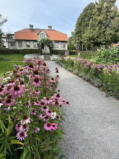 Garden path with pink flowers leading to Swedish house with orange roof