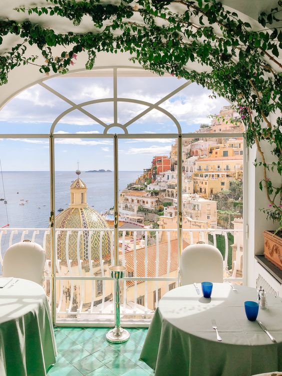 Arched window view of Positano coastal town with pastel buildings, sea, and ivy frame