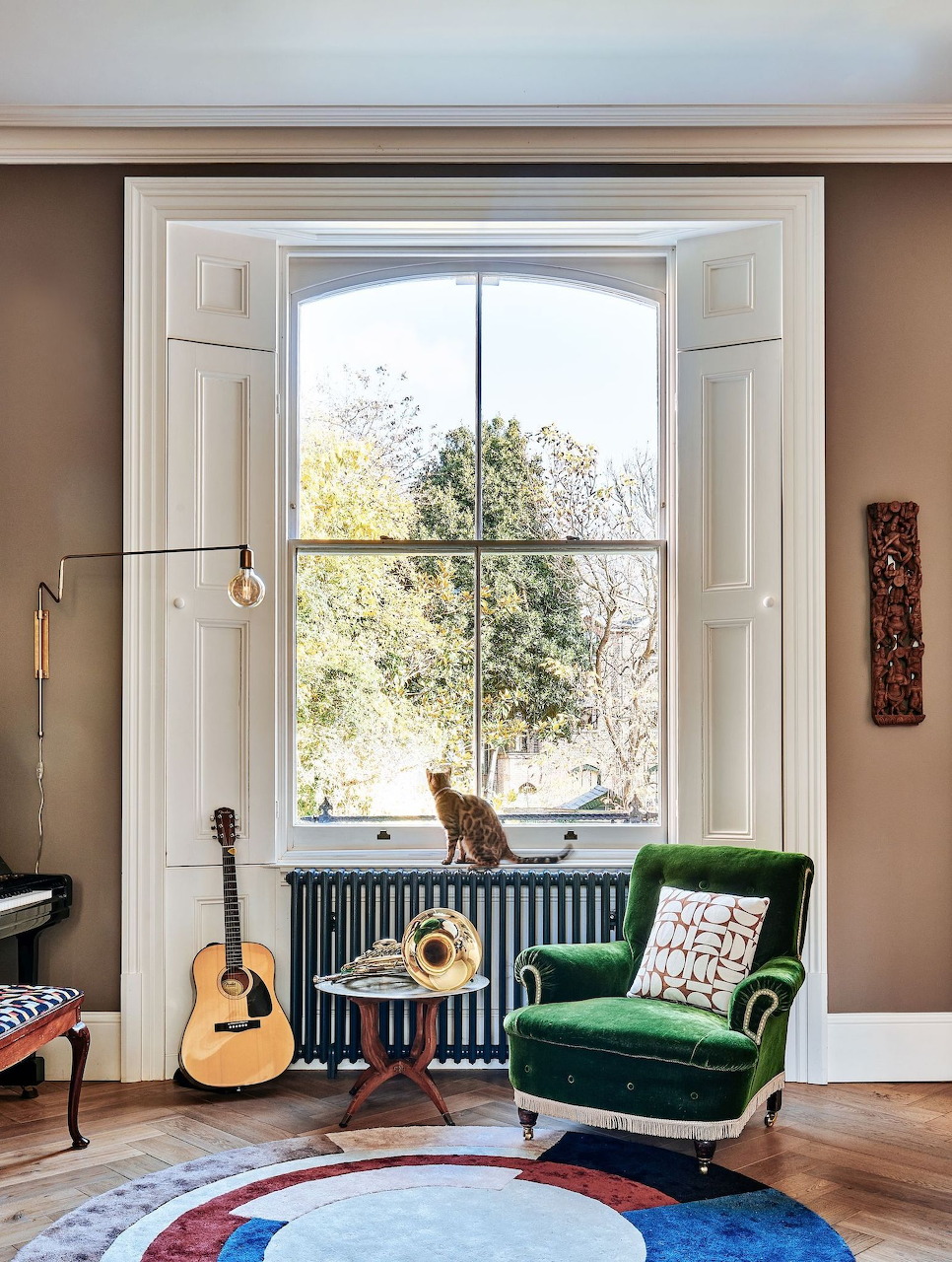 Cozy music room with a window, green chair, guitar, side table, and a cat by the radiator