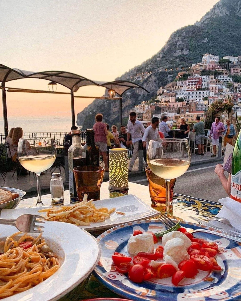 Sunset dining table with pasta, caprese salad, and wine overlooking Positano's colorful buildings and sea