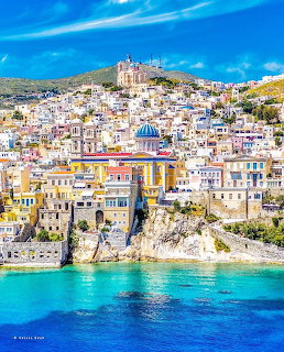 Colorful hillside town on Syros island with blue-domed church above turquoise sea