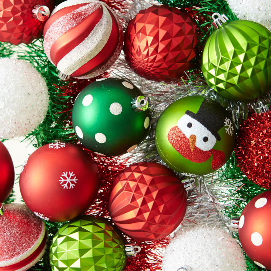 Assorted red, green, and white Christmas ornaments with geometric patterns and snowman design on silver tinsel