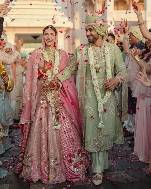 Bride and groom in traditional Indian wedding clothes walking under falling flower petals