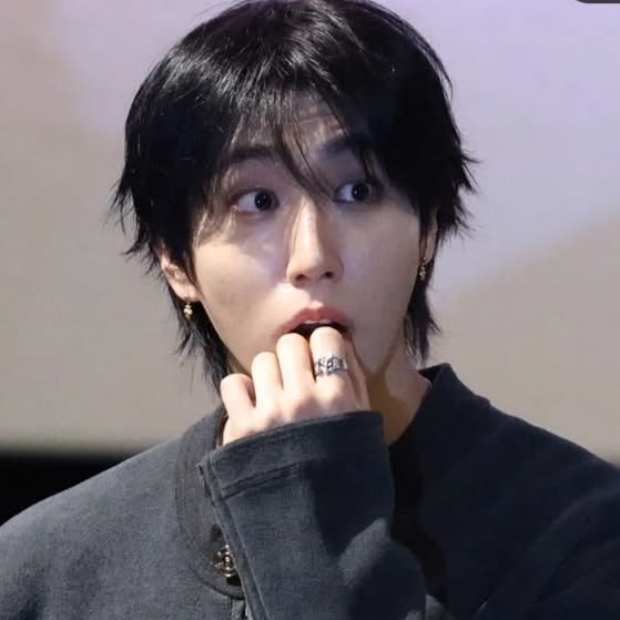 Portrait of young man with black hair and hand near his mouth wearing dark clothing