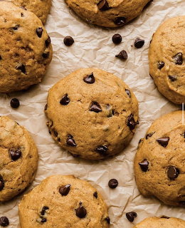 Golden brown chocolate chip cookies on crinkled parchment paper with loose chocolate chips