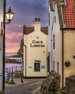 Narrow seaside lane with the Cod & Lobster building, old houses, a street lamp, and sunset sky